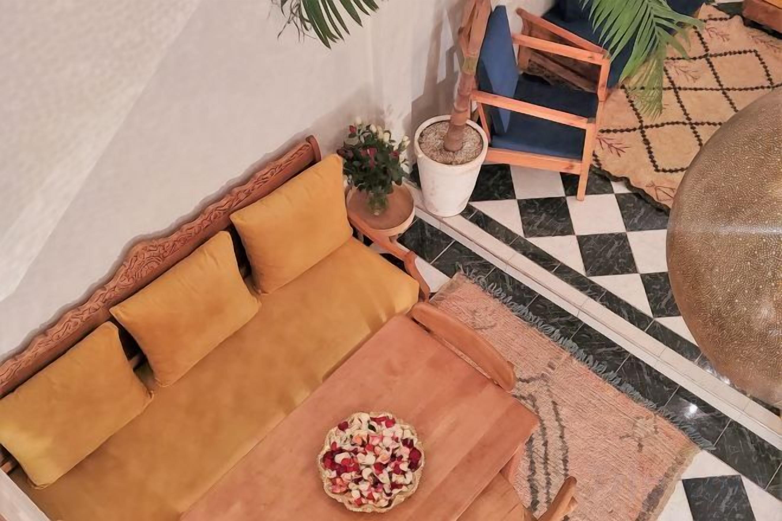 Une pièce avec un canapé, une petite table sur laquelle se trouve un saladier rempli de fruits, une plante en pot et un sol à carreaux.