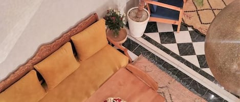A room with a sofa, a small table with a bowl of fruit, a potted plant, and a checkered floor.