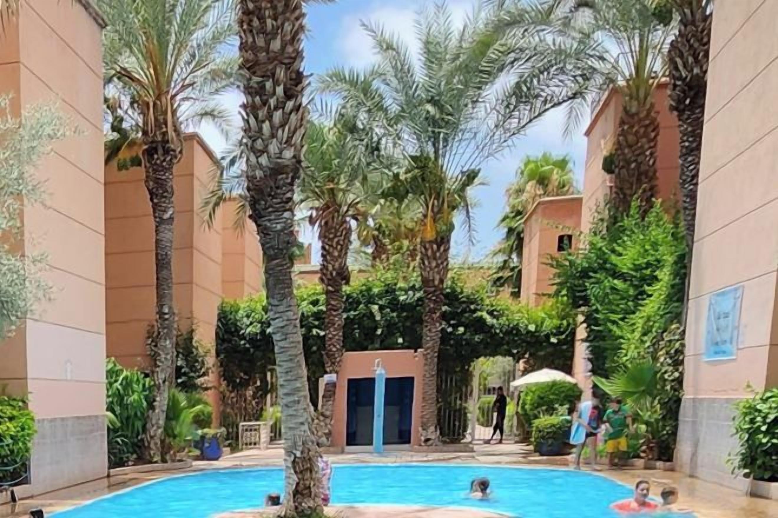 A pool area with palm trees, a building entrance, and a person in the water.
