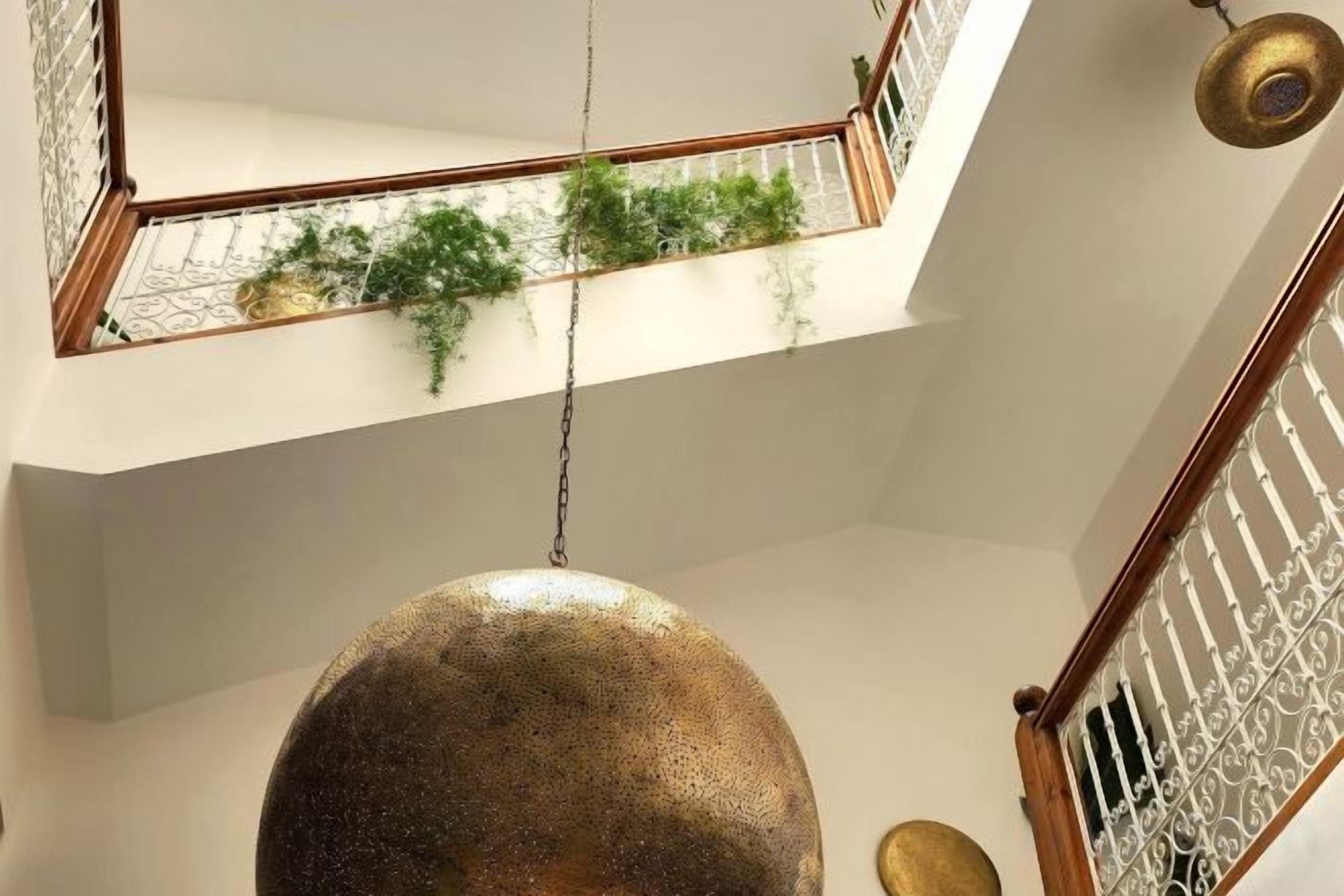 Una lámpara esférica colgante en un espacio interior de varios niveles, con una escalera y un balcón con vegetación.
