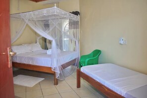 A room with two beds, one with a canopy and one without. There is a green chair and a small table. - Stay happy at Raz Homes (Diani Beach)