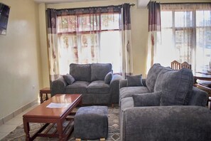 A living room with a sofa set, a wooden coffee table, and a patterned rug. - Stay happy at Raz Homes (Diani Beach)