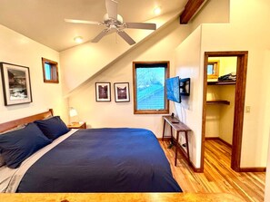 Une chambre à coucher avec un lit, un ventilateur de plafond, une télévision et un plancher en bois.