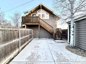 Une maison à deux étages avec une terrasse en bois, un escalier menant à l’étage supérieur et une cour arrière clôturée.