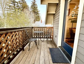 Une terrasse en bois avec une rambarde en treillis, deux tables en métal et une porte dotée d’un panneau de verre.
