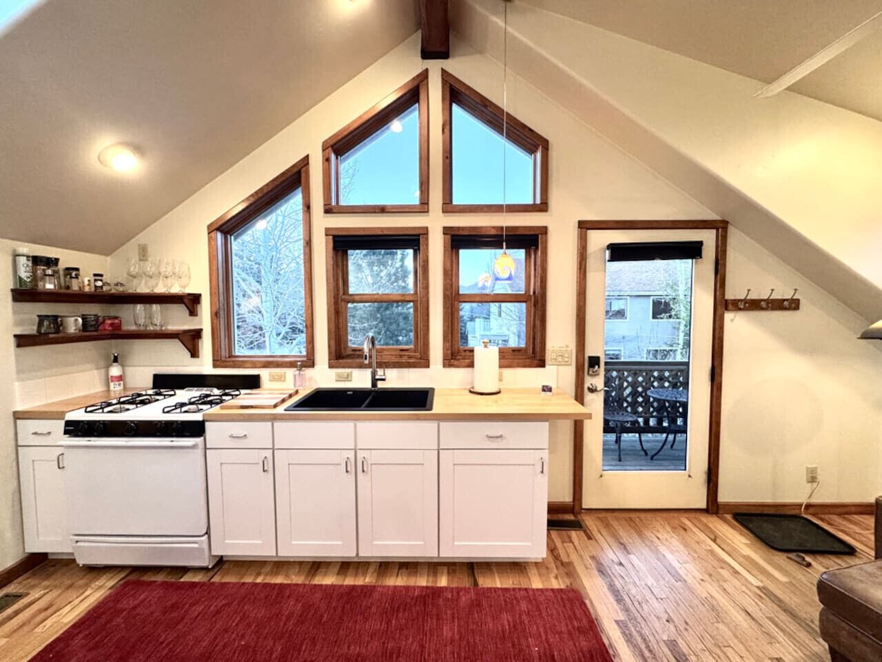 A kitchen with a gas stove, white cabinets, a red rug, and a large window with a view of trees.