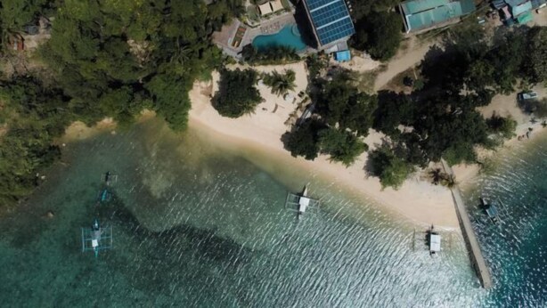 An aerial view of a coastal property with a swimming pool, solar panels, and a beach. - Bugana Beach and Dive Resort (Negros Occidental)