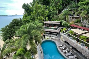 Un resort con piscina rodeada de exuberante vegetación y vista al mar.