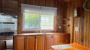 A kitchen with wooden cabinets, a stainless steel stove, a window with a white blind, and a wooden countertop. - Isla privada Mata Mua (Bocas del Toro)