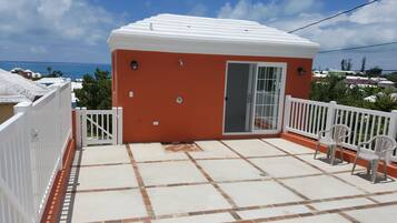 A small, orange building with a white roof and a sliding glass door, located on a balcony with a tiled floor and white railings.
