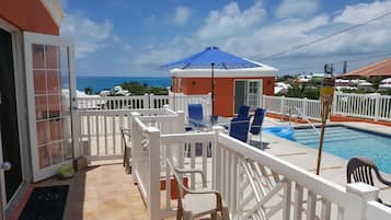 A pool area with a view of the ocean, white railings, and a blue umbrella.