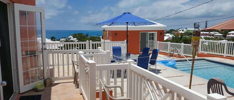 A pool area with a view of the ocean, white railings, and a blue umbrella.