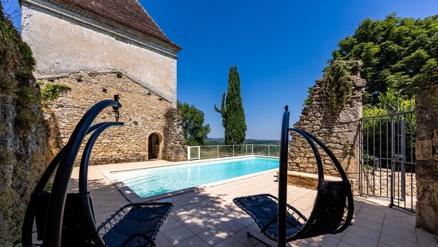 Una piscina con sillas de descanso, un edificio de piedra y un cielo azul despejado.