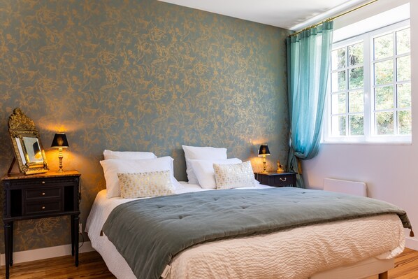 A bedroom with a bed, nightstands, lamps, a window with curtains, and a patterned wall. - Florence Room — Italian Elegance and Modern Comfort (Puybarban)