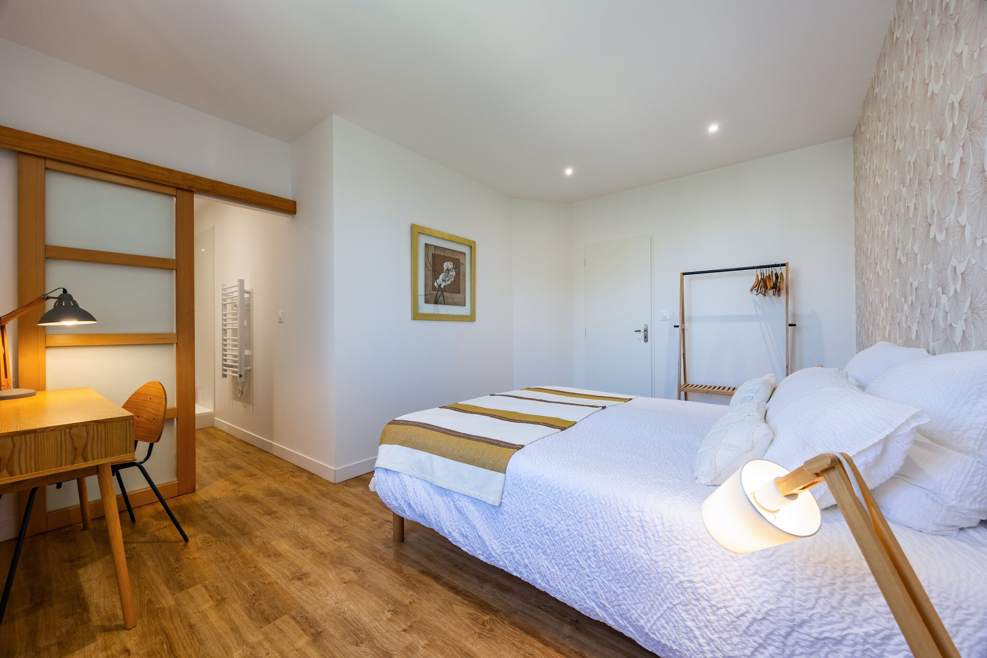 Une chambre à coucher comprenant un lit, un bureau, une chaise, une lampe, une armoire et un tableau encadré accroché au mur.