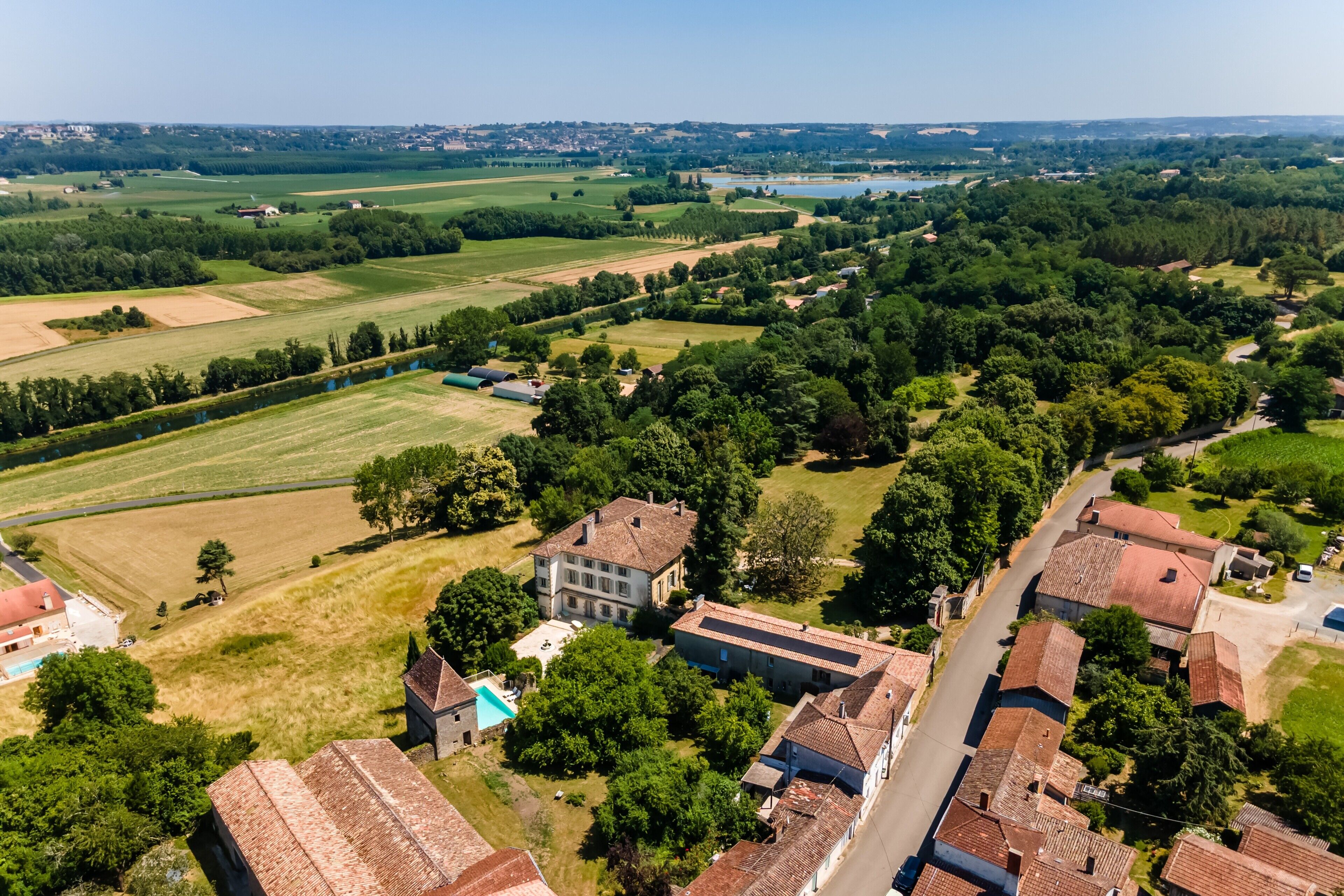 An aerial view of a rural village with traditional buildings, open fields, and a small body of water.