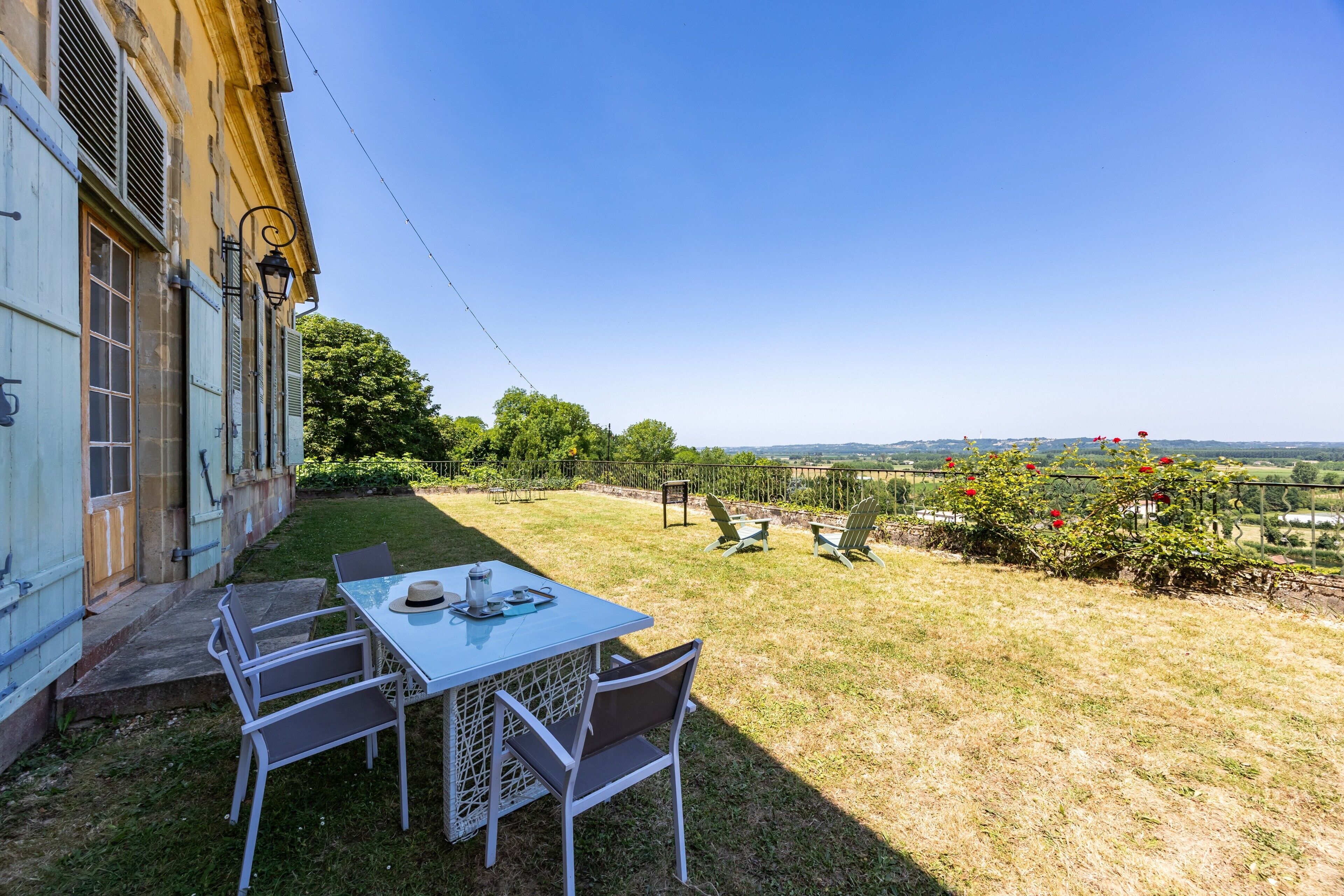 Eine Terrasse mit Tisch und Stühlen, ein Gebäude mit einem Fenster und Blick auf die Landschaft.