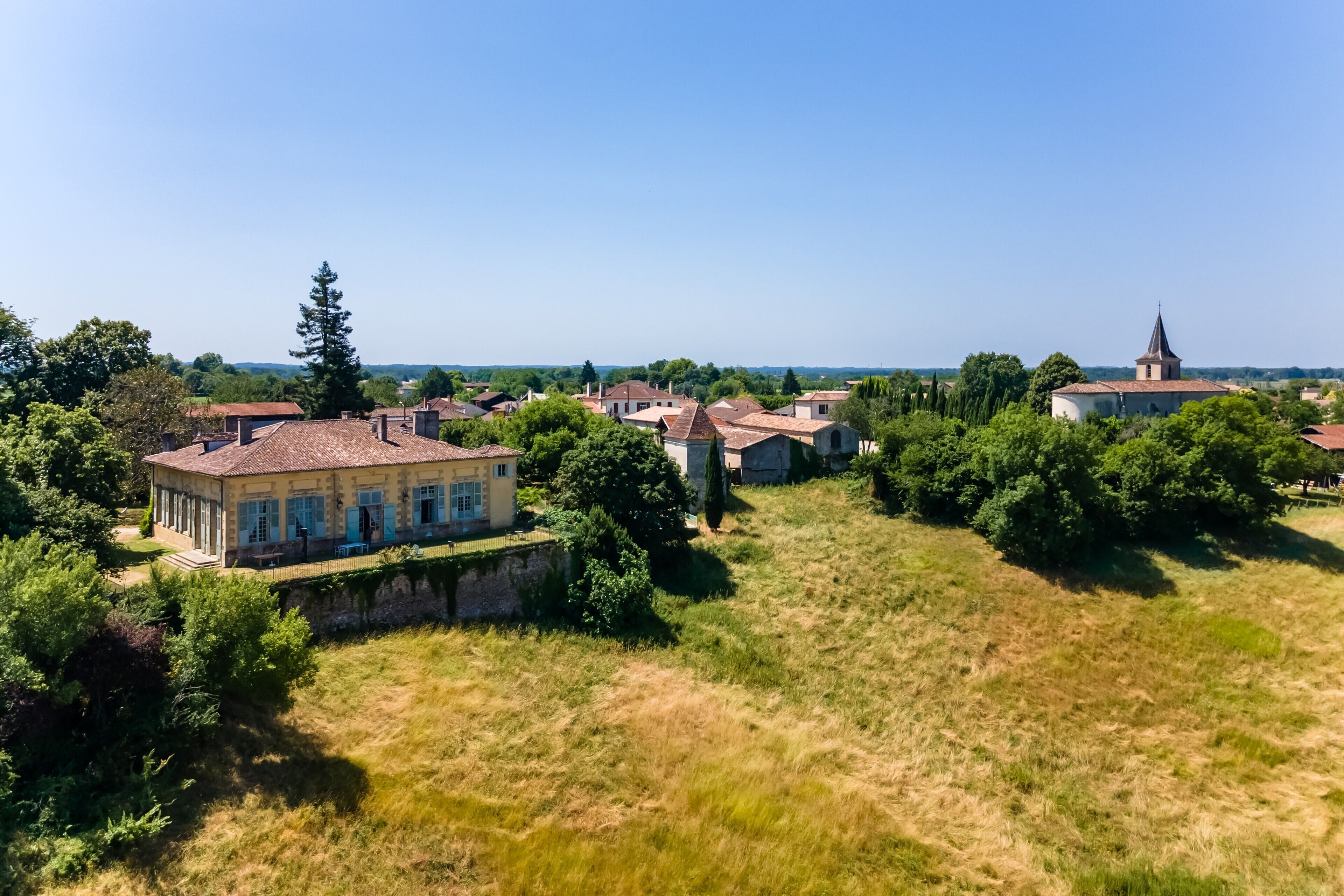 Un village rural avec des bâtiments traditionnels, une église et une grande maison dotée d’un jardin.