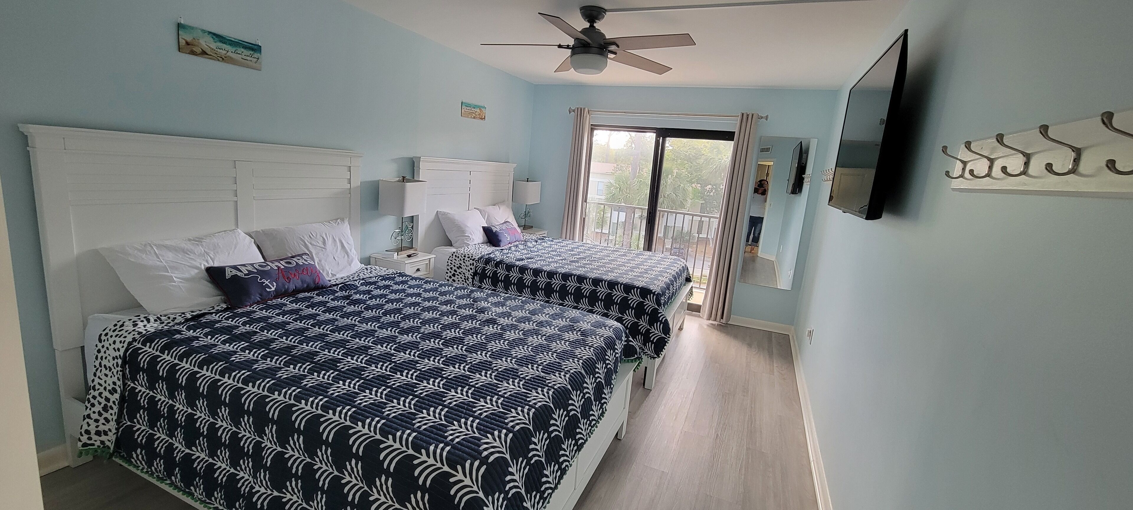 A bedroom with two beds, a ceiling fan, a TV, and a balcony with curtains.