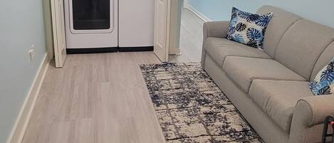 A compact living space with a kitchenette, a beige sofa, and a patterned rug.