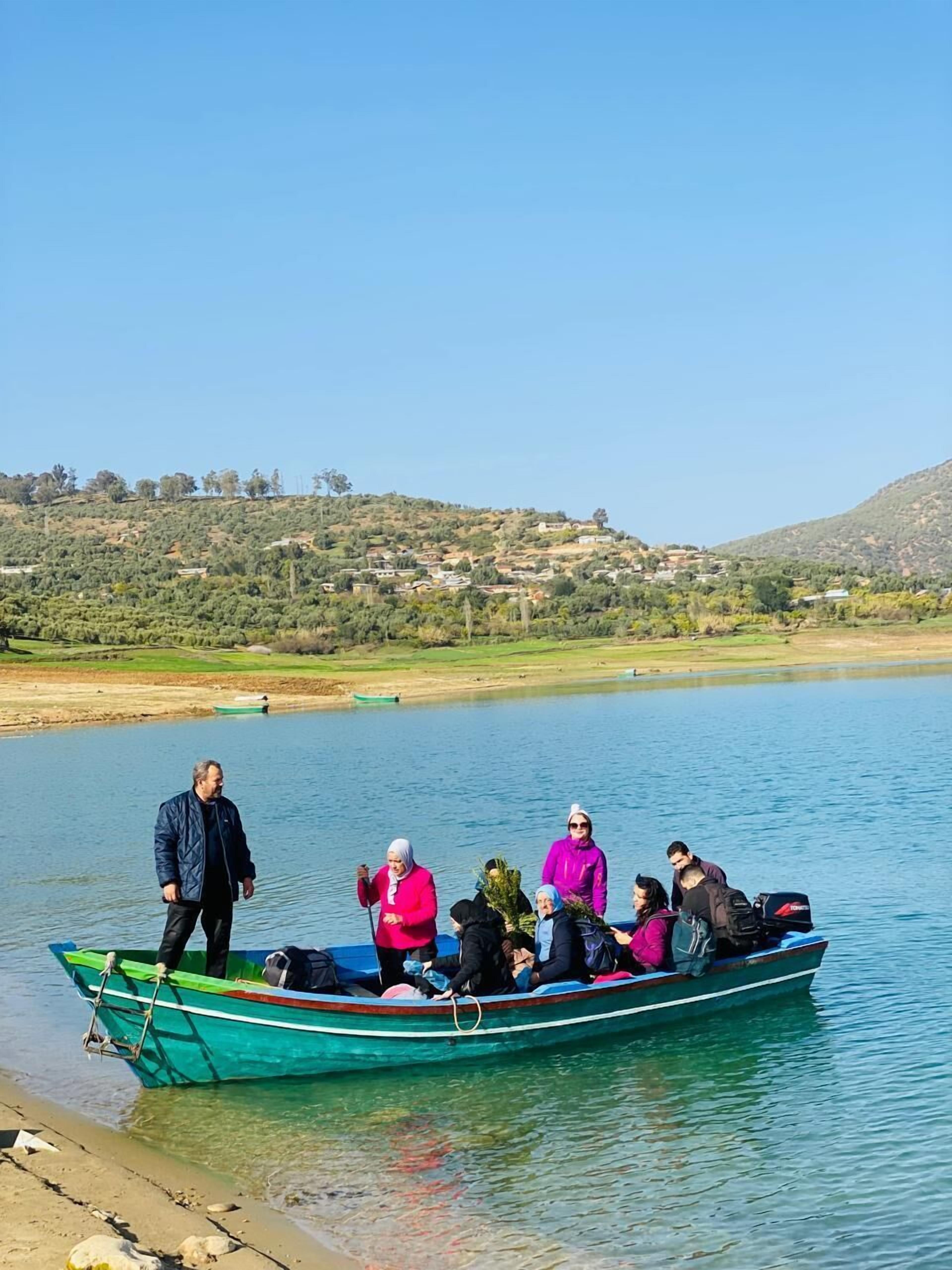 A group of people on a boat near a calm lake with a hilly landscape in the background.