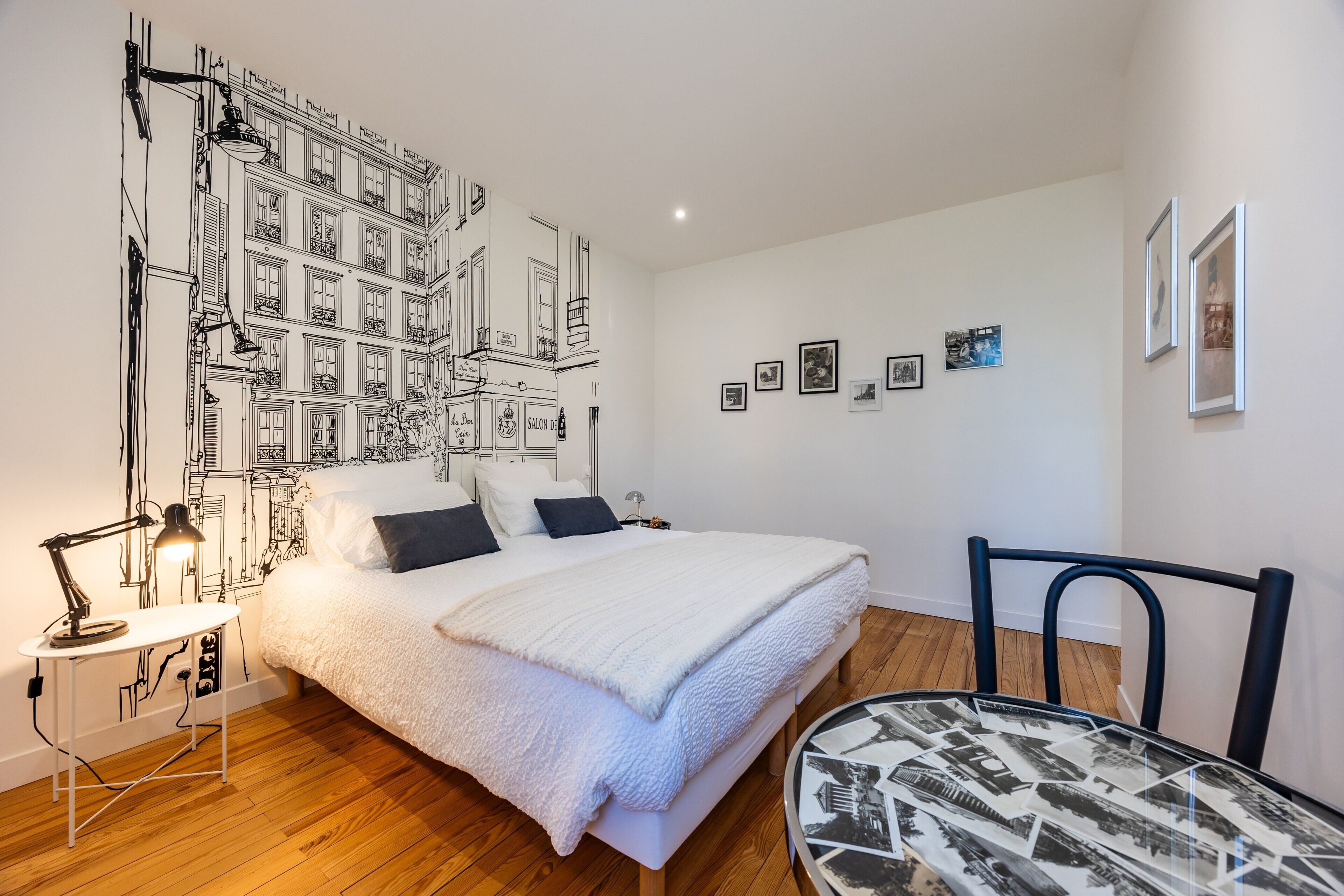 Ein Schlafzimmer mit einem Bett, einem Schreibtisch mit Lampe, einem Sessel und einer Wand mit gerahmten Bildern.