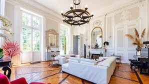 Een ruime kamer met een grote witte bank, een rode fauteuil en een kroonluchter.