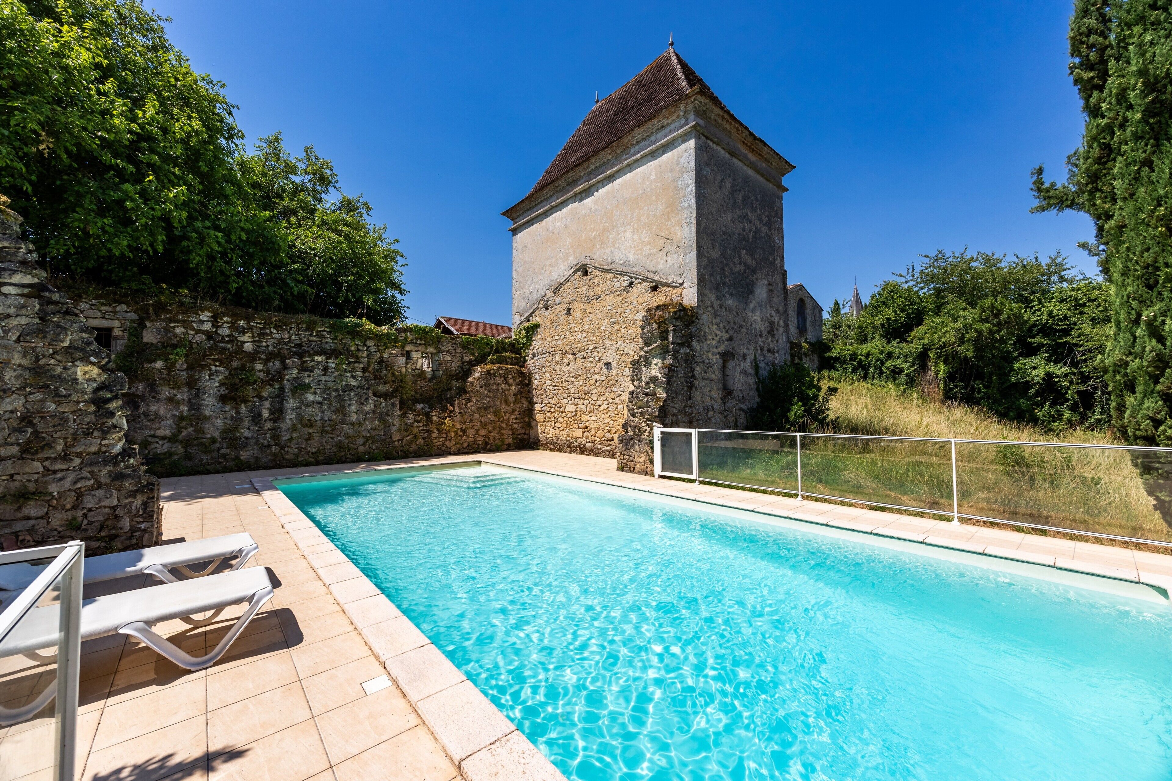 Una piscina con sillones de descanso, una pared de piedra y un edificio con techo a dos aguas.