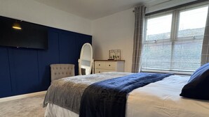 Ein Schlafzimmer mit einem Bett, einem Schminktisch, einem Spiegel und einem an der Wand befestigten Fernseher.