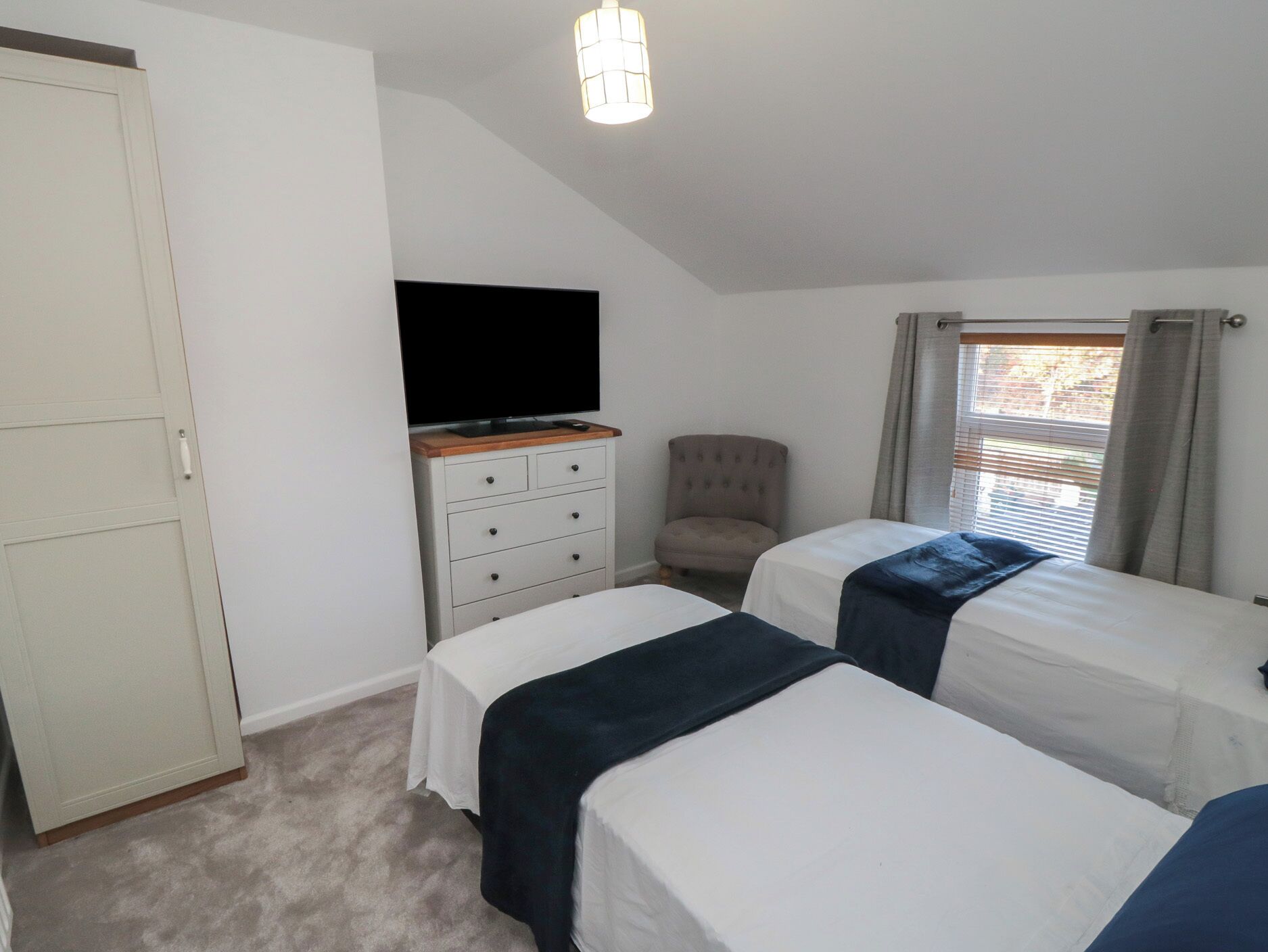 A bedroom with two beds, a television on a dresser, a chair, and a window with curtains.