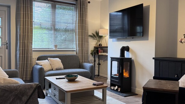Ein gemütliches Wohnzimmer mit einer Couch, einem Couchtisch, einem Kamin und einem an der Wand montierten Fernseher.