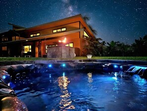 Une maison moderne avec une piscine, de nuit, sous un ciel étoilé.