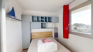 Ein Schlafzimmer mit Bett, Kleiderschrank, Regalen und einem Fenster mit rotem Vorhang.