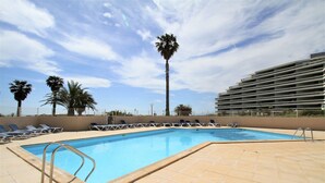 Ein Pool mit Liegestühlen und Palmen, umgeben von einem modernen Gebäude.