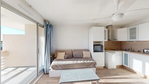 Ein kompakter Wohnbereich mit einer Couch, einem kleinen Tisch, einer Küchenzeile und einer Schiebeglastür zum Außenbereich.