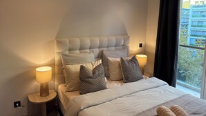 Une chambre avec un grand lit, deux lampes de chevet et une vue sur un immeuble par la fenêtre.