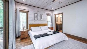 A bedroom with a wooden ceiling, a bed with white bedding, a nightstand, a dresser, and a window with curtains. - Modern Getaway: Hot Tub, Pool Table, Arcade & Fire Pit (Blue Ridge)