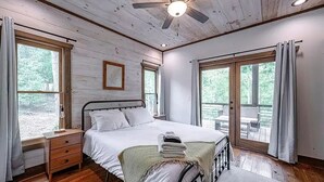 A bedroom with a wooden ceiling, a bed with white linens, a nightstand, and a window with curtains. - Modern Getaway: Hot Tub, Pool Table, Arcade & Fire Pit (Blue Ridge)