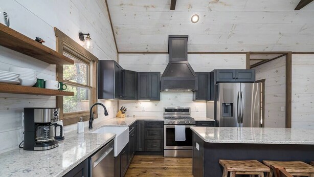 A modern kitchen with dark cabinets, a stainless steel refrigerator, and a coffee maker. - Modern Getaway: Hot Tub, Pool Table, Arcade & Fire Pit (Blue Ridge)