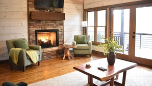 A cozy living room with a fireplace, two armchairs, a coffee table, and a large window. - Modern Getaway: Hot Tub, Pool Table, Arcade & Fire Pit (Blue Ridge)