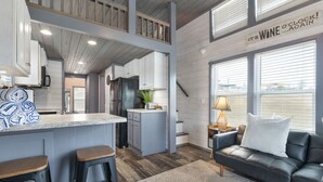 Een moderne keuken met een centraal eiland, een zithoek met een bank en een groot raam met jaloezieën.