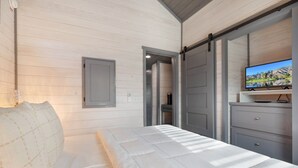 Een slaapkamer met een bed, een televisie op een dressoir en een deur naar een andere kamer.