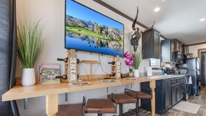 Una cucina moderna con una barra in legno, sgabelli da bar, un grande televisore e una dispensa per vini a parete.