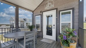 A covered outdoor area with a table and chairs, a wooden planter with flowers, and a door with a welcome mat. - The Grape Escape (Fredericksburg)