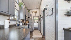 A narrow kitchen with a central island, wooden flooring, and a view into the adjacent bedroom. - The Grape Escape (Fredericksburg)