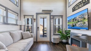 A cozy living room with a sofa, a television, a fireplace, and a door leading outside. - The Grape Escape (Fredericksburg)