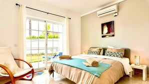 A bedroom with a bed, a rocking chair, a nightstand, and a view of the outdoors. - Casa Luna with Saltwater Pool – Private Pool, Garden & Parking (Olhos de Água)