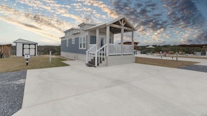 A single-story building with a porch, a small attached structure, and a clear sky with clouds. - Little Blue Haus with Hot Tub! (Fredericksburg)