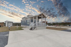 A single-story building with a porch, a small attached structure, and a clear sky with clouds. - Little Blue Haus with Hot Tub! (Fredericksburg)