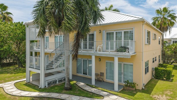 A two-story building with a balcony on the upper floor, surrounded by palm trees and a landscaped garden.